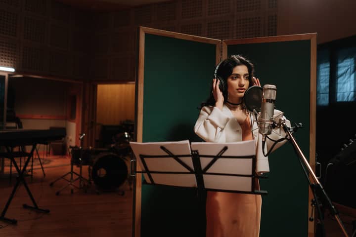 Woman singing into a microphone in a music studio with headphones.