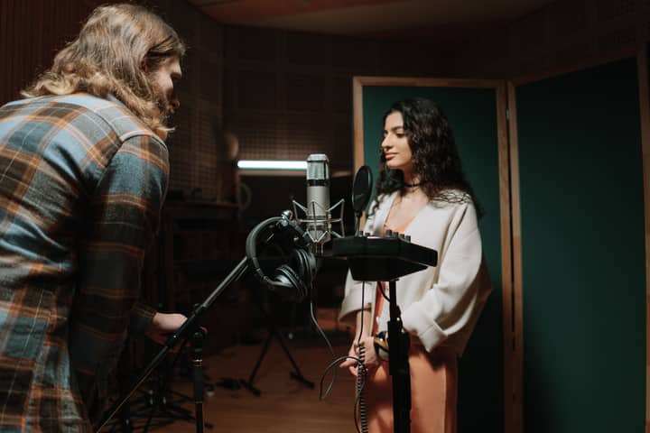 A woman recording vocals in a professional music studio setting.