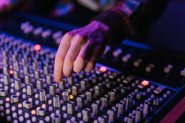 Close-up of a hand adjusting audio mixer sliders under neon lighting.