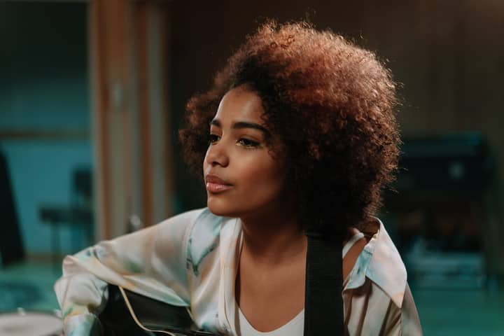 Close-up of a black woman musician with afro hair playing guitar indoors.