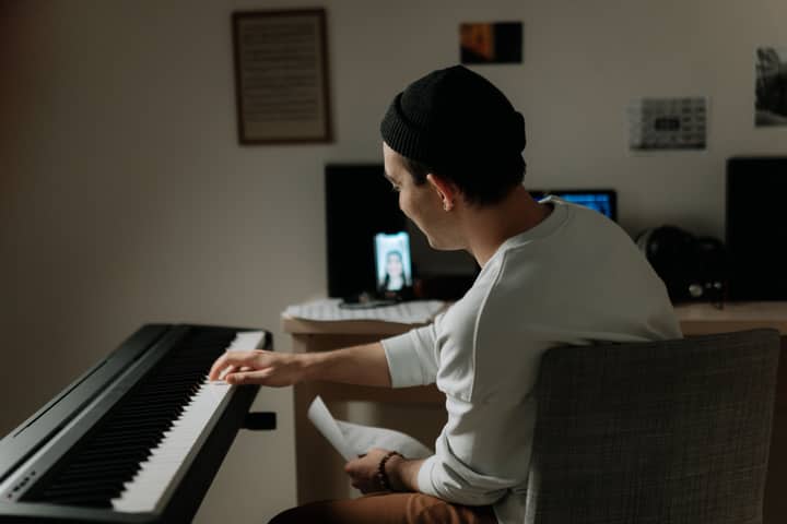 A man in a home studio playing the piano during a virtual lesson, showcasing leisure and creativity.
