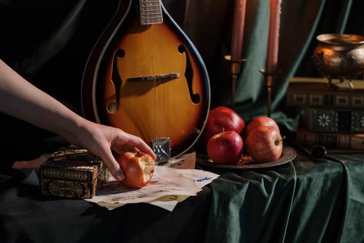 Artistic still life featuring a mandolin, apples, and candles on a table.
