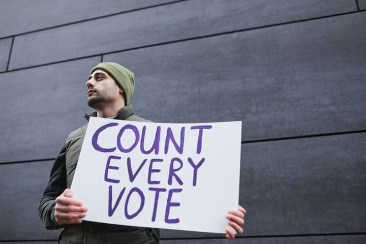A man holding a 'Count Every Vote' placard, promoting democracy and voting rights.