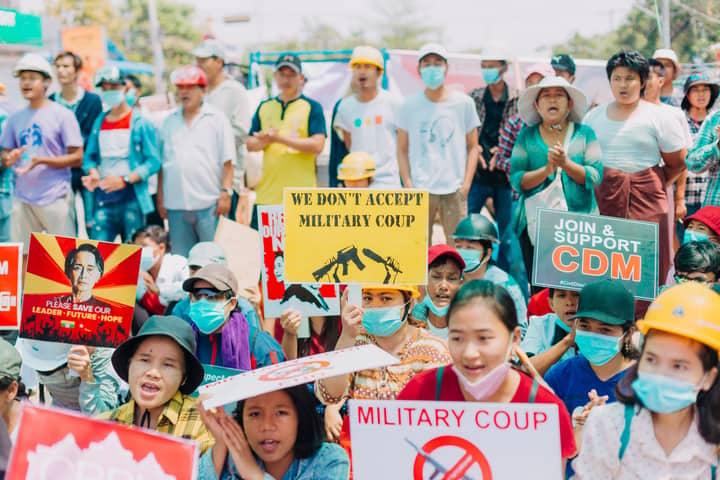 Large crowd in Yangon protests peacefully against military coup, holding signs and wearing face masks.