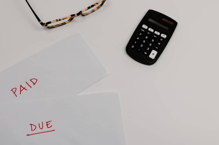 Top view of financial papers labeled 'Paid' and 'Due' beside a calculator and glasses.