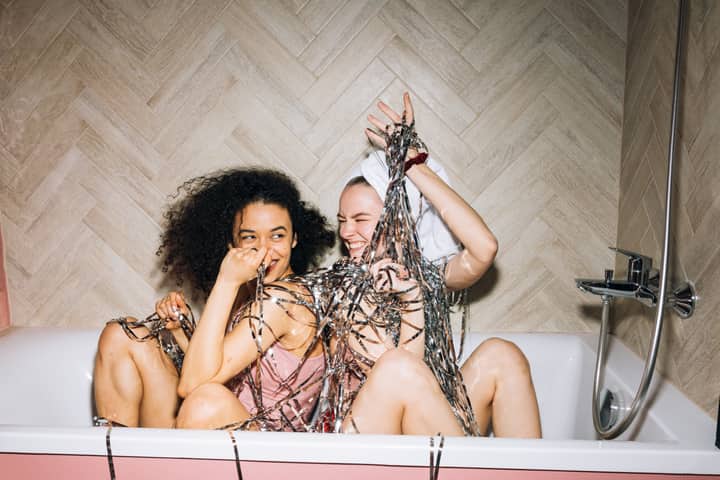 Two young women having fun in a bathtub, laughing and enjoying a fun-filled moment.