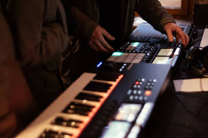 Music producer using synthesizer and beat pad in studio setting.