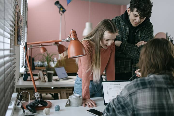 A group of young adults engage in a team meeting in a modern office, discussing ideas around a laptop.