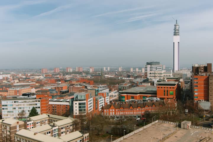 Tall industrial tower located amidst abundance of colorful residential houses with windows located on streets of city against blue sky