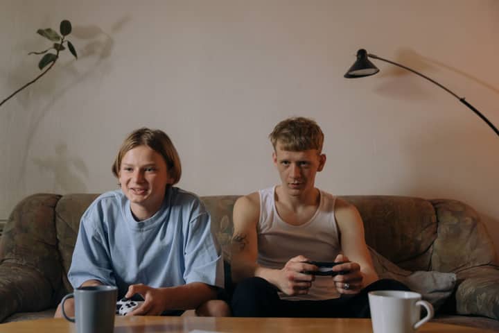 Two young men engaging in gaming on a sofa, enjoying a relaxed indoor setting.