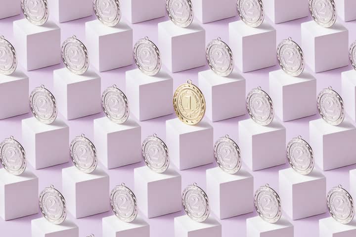 A gold medal stands out among silver medals on white cubes, showcasing uniqueness.