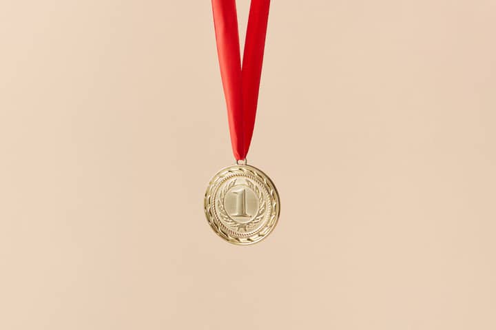 Close-up of a gold medal with a red ribbon on a beige background, symbolizing achievement.