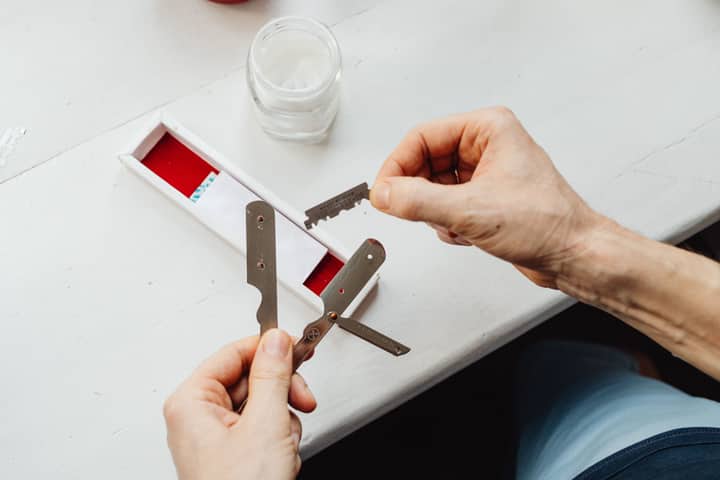 Close-up of hands assembling razor blades on a white table in natural light.