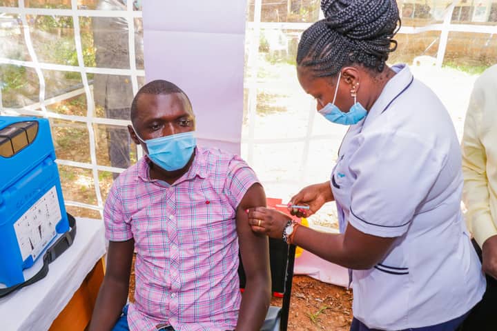 A nurse gives a COVID-19 vaccination to a man at an outdoor health facility.