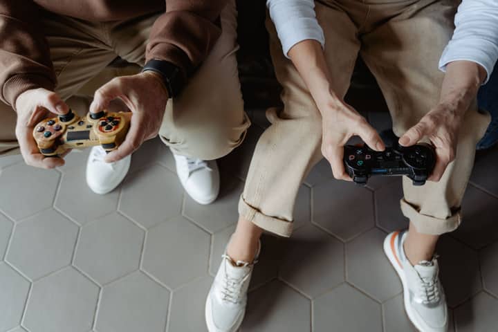 Two adults playing video games with controllers while seated on a sofa, having fun indoors.
