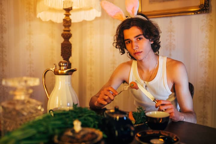 A young man wearing bunny ears enjoys a meal in a warmly lit, elegantly decorated setting.