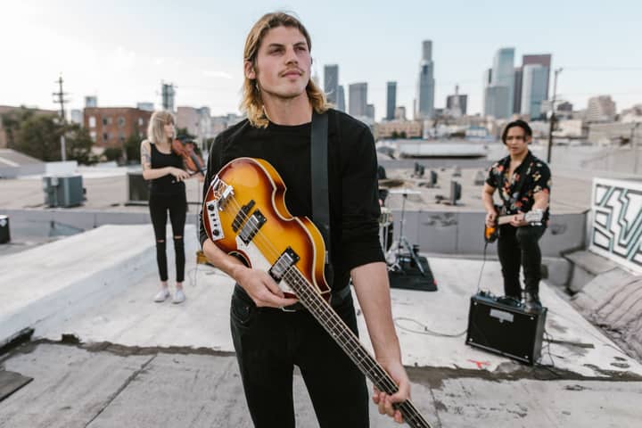 Musicians playing guitar and violin on a rooftop with city skyline backdrop.