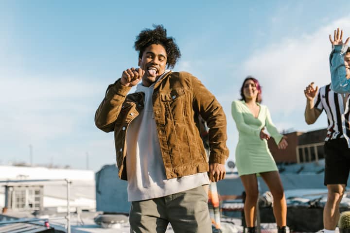 Group of friends dancing cheerfully on a rooftop, enjoying a sunny day together.