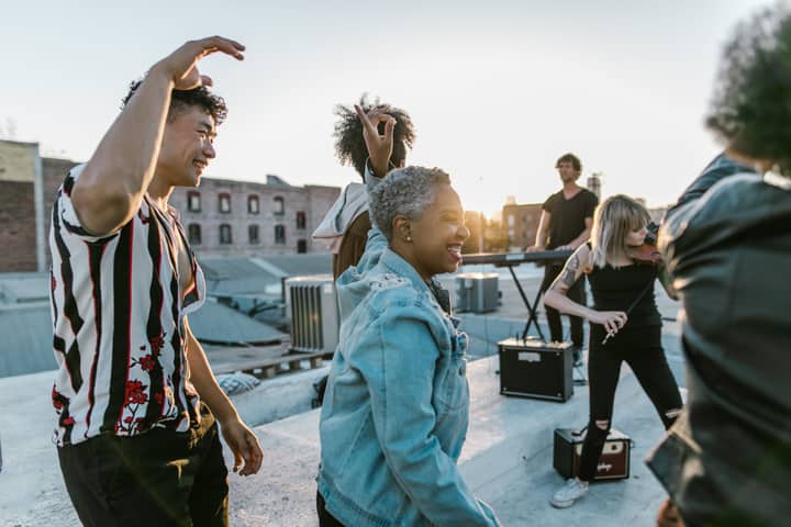 Group of musicians enjoying a lively rooftop dance party at sunset, creating a joyful atmosphere.