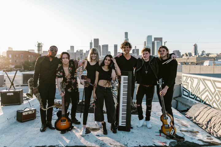 A diverse music band performing on a rooftop with a city skyline backdrop during sunset.