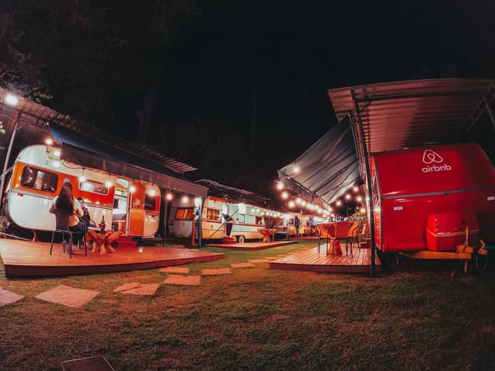 Travelers having picnic near caravan located at camping area among tall trees at night
