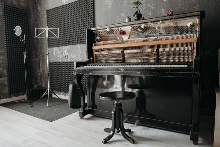 An open vintage upright piano in a soundproof music studio with recording equipment.