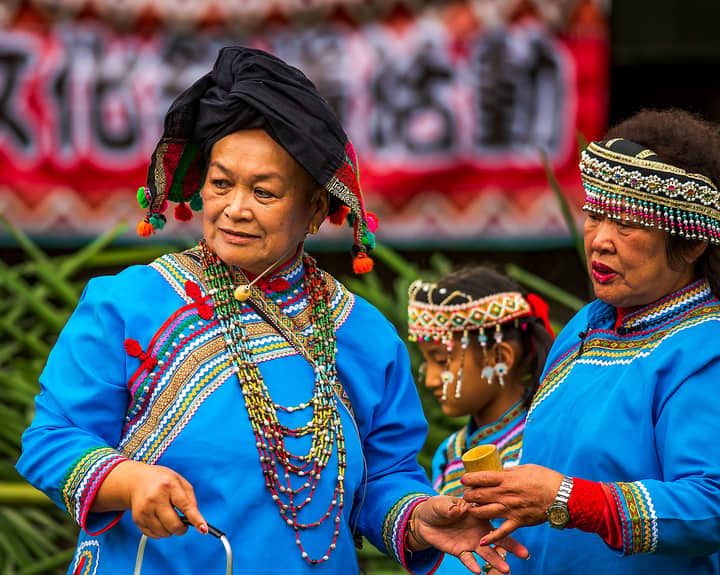 Elderly Taiwanese women in vibrant traditional attire participating in a cultural festival outdoors.