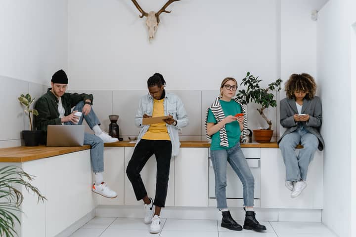 Casual and diverse colleagues using gadgets in a modern office kitchen area.