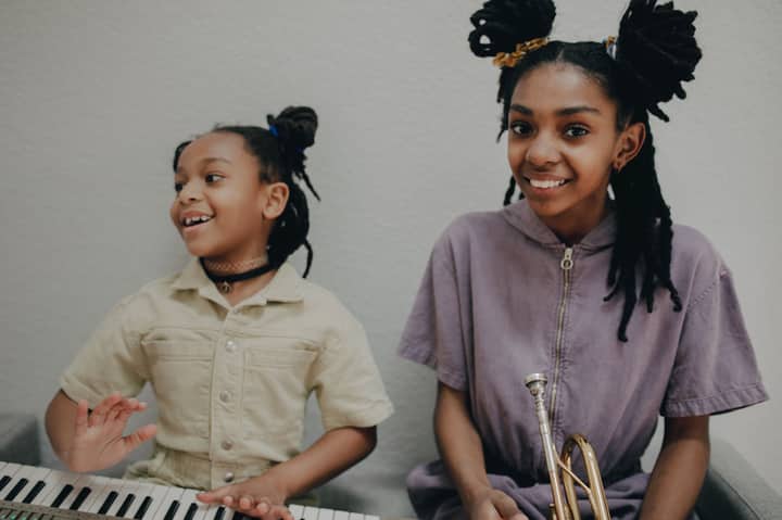 Happy siblings enjoying playing the keyboard and trumpet indoors, showcasing musical talent.