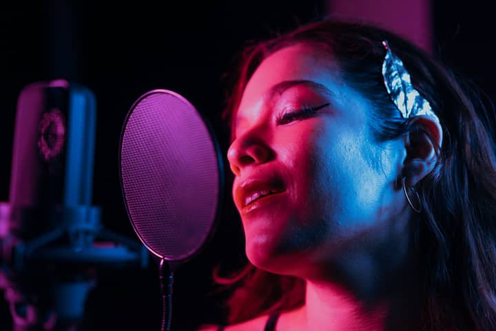 Close-up of a woman passionately singing into a studio microphone with vibrant lighting.