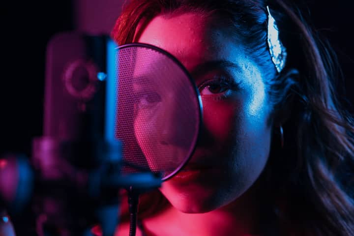 A close-up of a female singer in a recording studio with vibrant lighting and a condenser microphone.