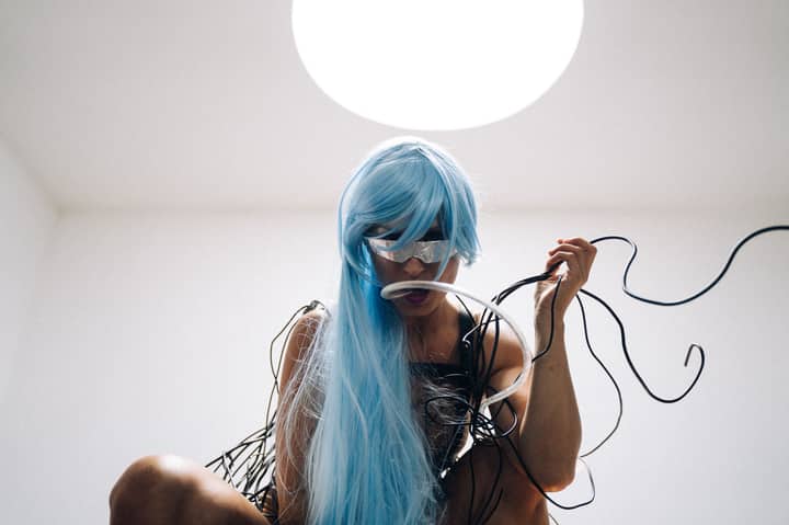 A woman in a cyberpunk outfit with blue hair and wires, embodying a futuristic concept.