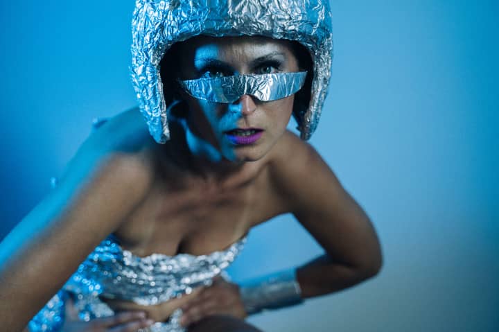 A futuristic-themed woman in metallic attire posing under blue lighting in a studio setting.