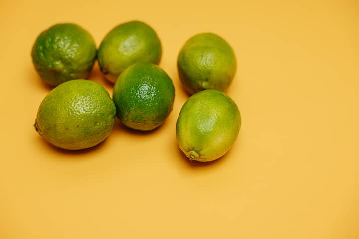 Six fresh green limes arranged on a vibrant yellow background, emphasizing freshness and citrus zest.