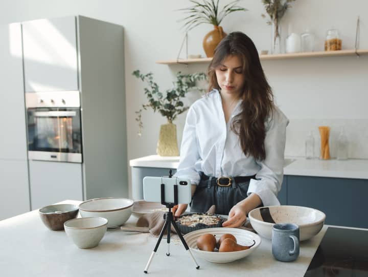 A woman cooking in a stylish kitchen while recording a vlog.