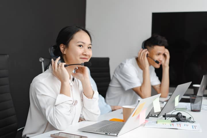 A diverse group of call center agents working with laptops and headsets in a modern office.