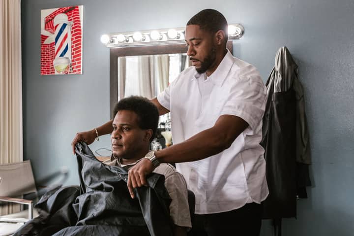 Professional barber drapes apron on client in stylish salon, preparing for a haircut session.