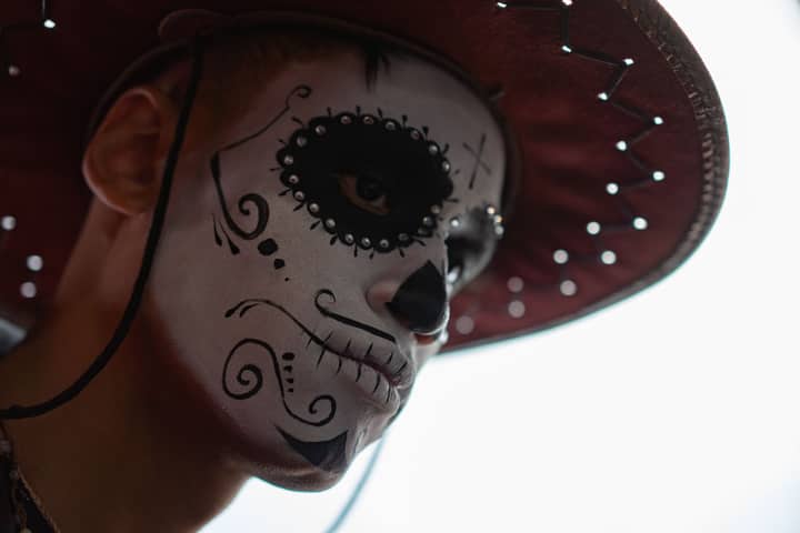 Close-up portrait of a person with Day of the Dead face paint wearing a hat, depicting a spooky and artistic look.