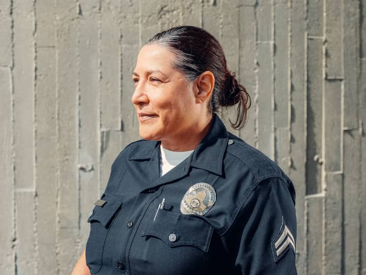 Portrait of a confident female police officer in uniform, standing outdoors against a textured wall.