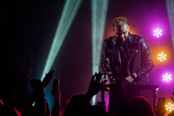 Live DJ performance with vibrant lighting, capturing the audience's excitement at an indoor concert.
