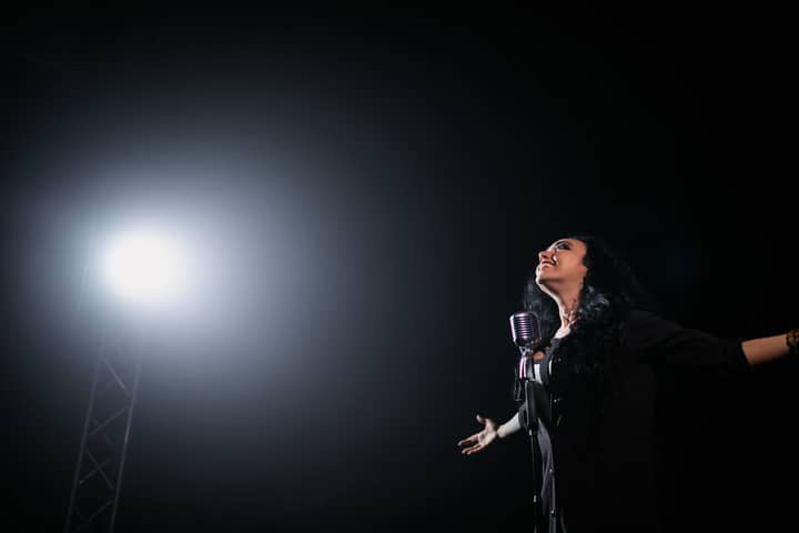 A passionate female singer performs on stage under a dramatic spotlight.