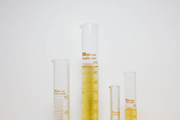 Close-up of graduated cylinders filled with yellow liquid in a laboratory setting.