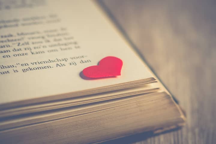 A red heart-shaped bookmark on the pages of an open book, symbolizing love.