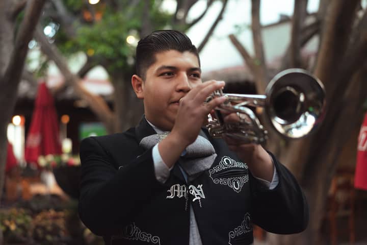 A mariachi musician plays the trumpet in traditional attire, showcasing Mexican culture outdoors.