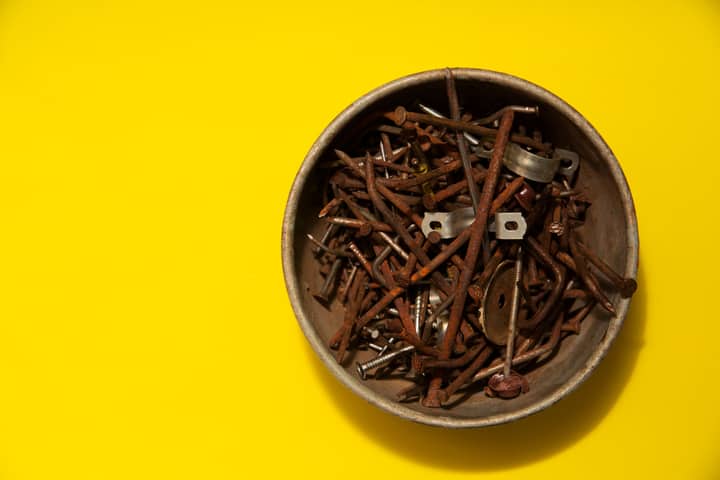 A bowl filled with assorted rusty nails on a vivid yellow background, top view.