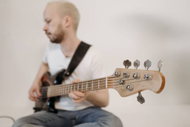 Young man playing a bass guitar indoors, focused on the instrument's headstock.