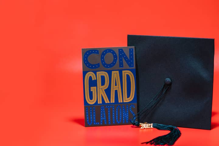 A stylish graduation card and cap on a vibrant red background, ideal for celebration themes.