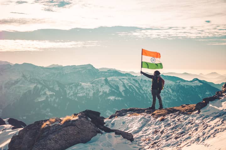 A hiker holding the Indian flag on a snowy mountain ridge, showcasing the majestic Himalayas.