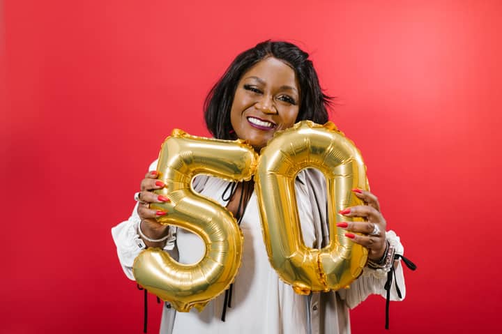 Smiling woman holding golden number 50 balloons against red background.