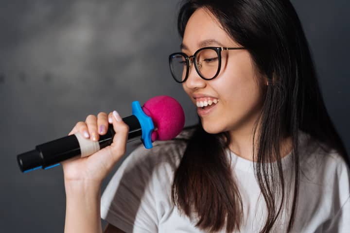 A young woman happily sings into a microphone during a karaoke session indoors.
